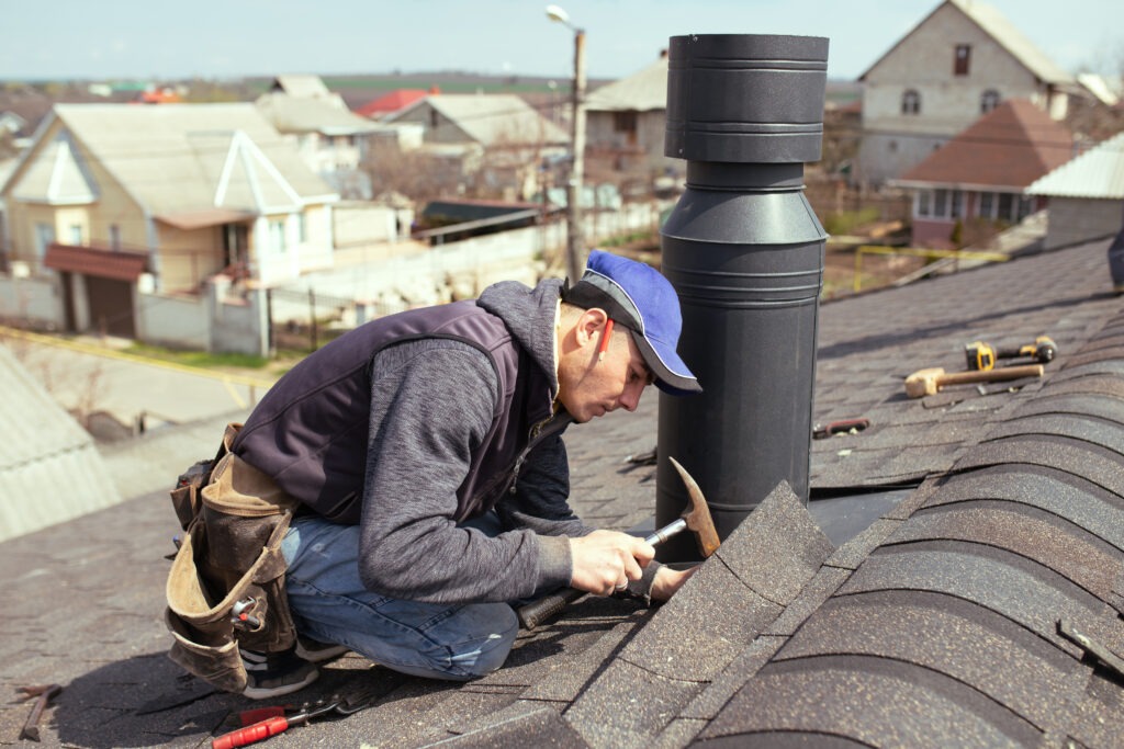 Roofer hammering down asphalt shingle roof.